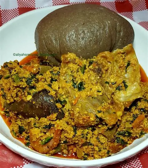 Close-up of Egusi soup in a bowl next to a serving of Amala on a wooden table